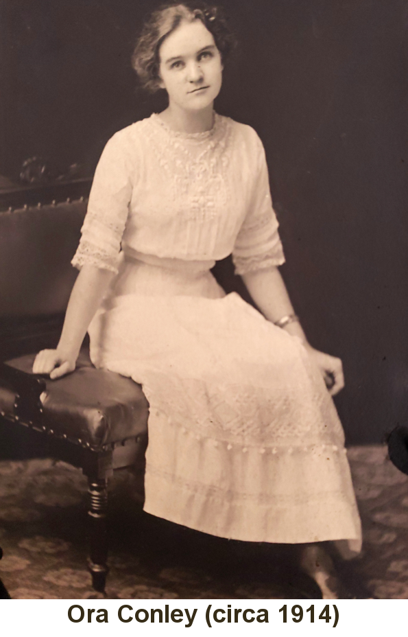 Sepia-tone photo of Ora Conley, in her early 20s, wearing a white dress and gold bracelet, hair bobbed, seated on a leather-upholstered armchair, in about 1914